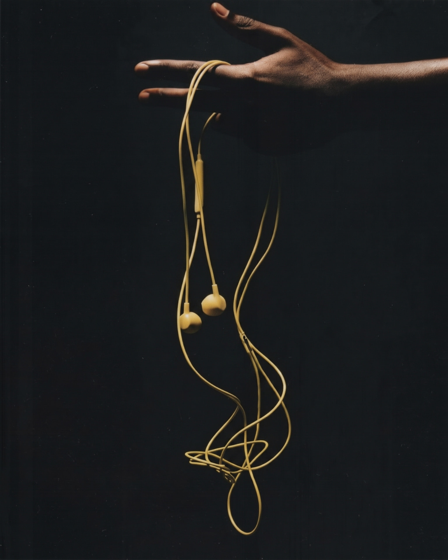 A hand holding a coiled pair of yellow wired earphones against darkness.