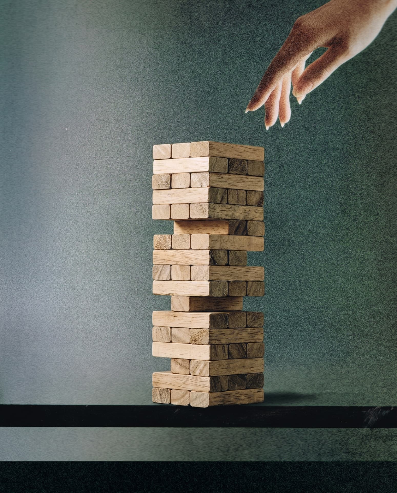 A hand reaching down toward a tower of wooden blocks on a dark shelf