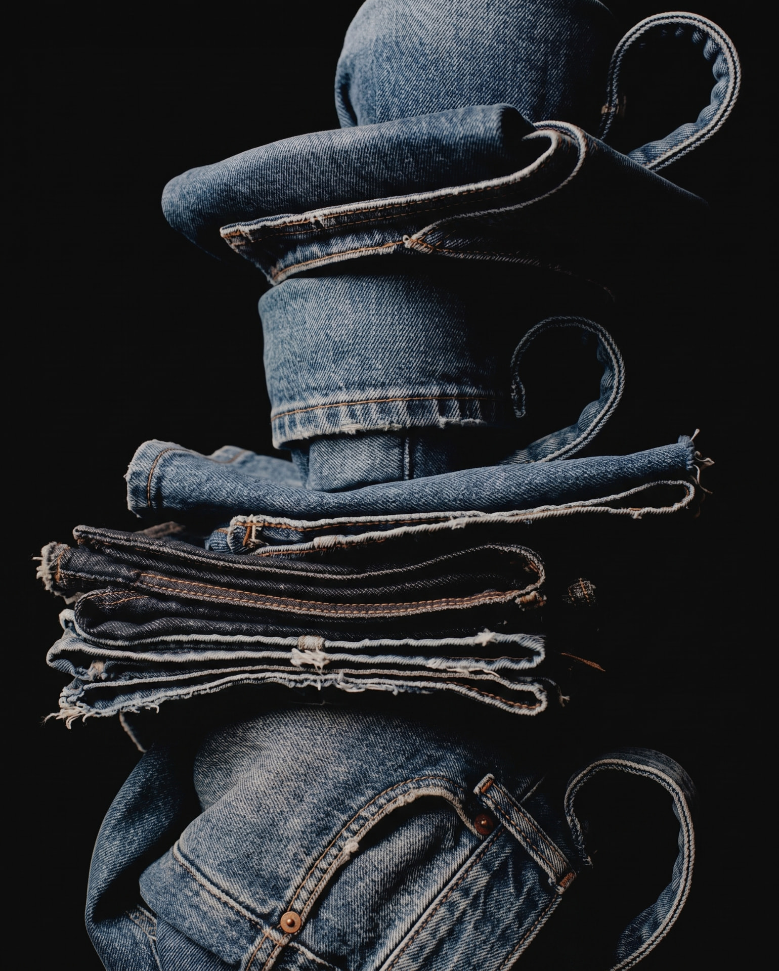 A stacked pile of folded denim jackets and jeans on a black ground.