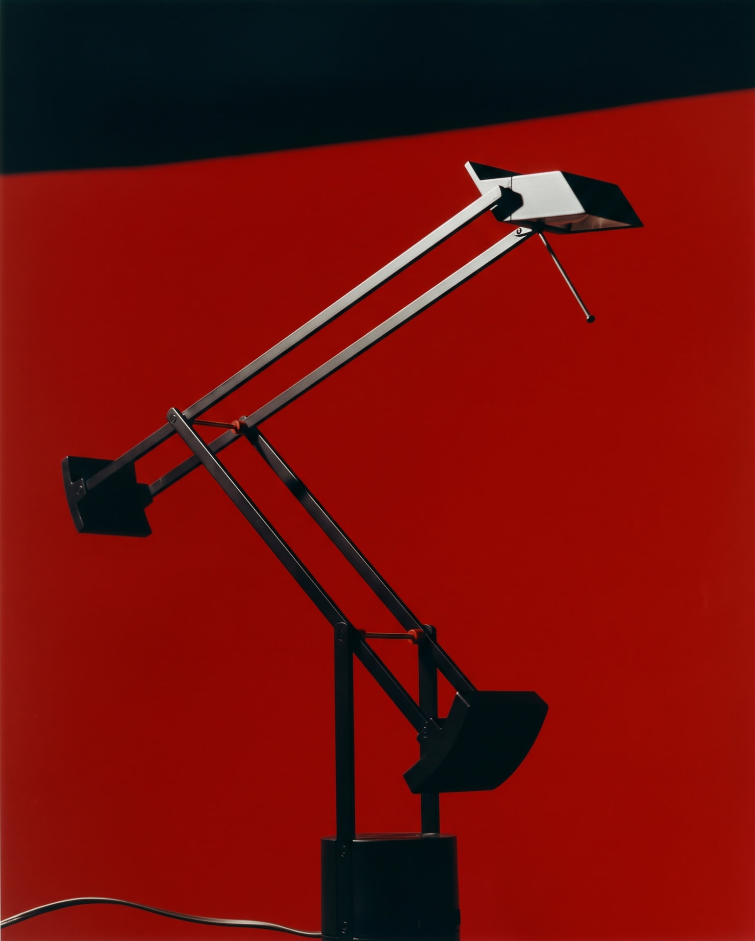 Black and red angular desk lamp photographed against a red ground.