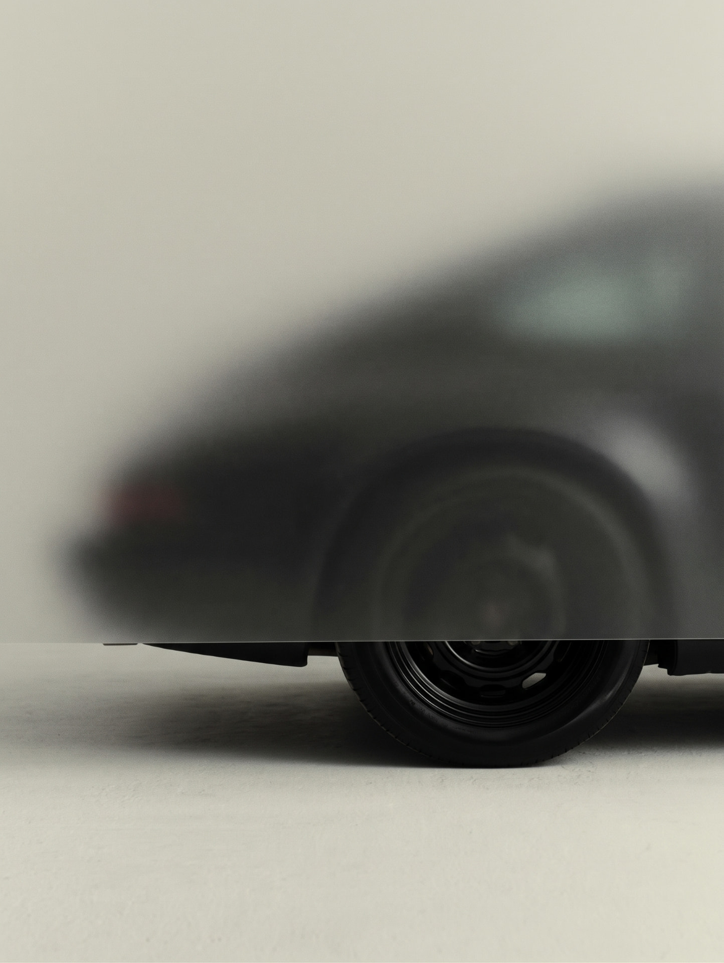 A car half covered by a translucent sheet, its front wheel resting on a pale floor.